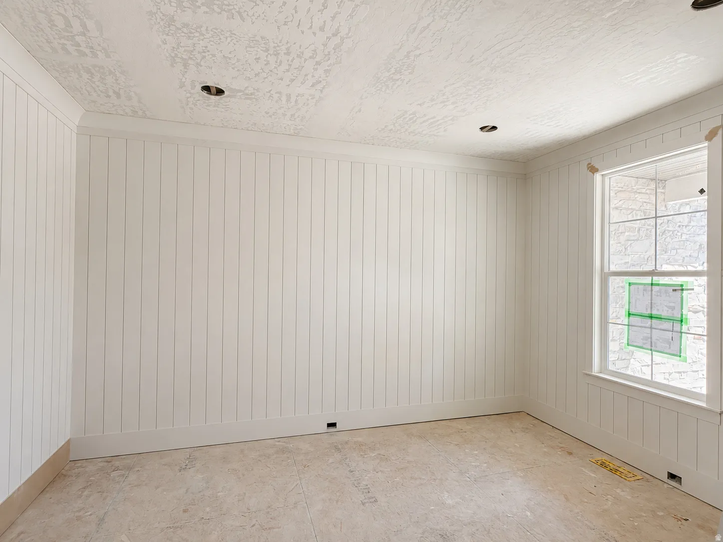 Room featuring vertical paneling, crown molding, and a single-hung window with a paneled apron