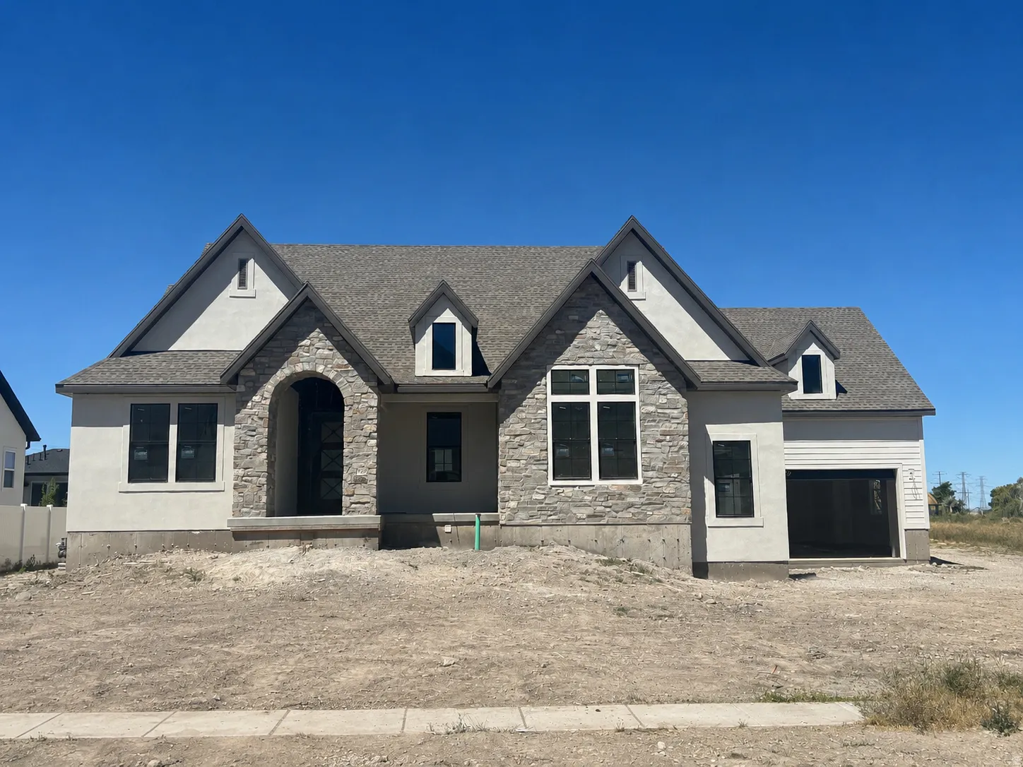 Contemporary exterior featuring a stone and stucco facade, an arched entry, a dark shingle roof, multiple dormer windows, and a two-car garage