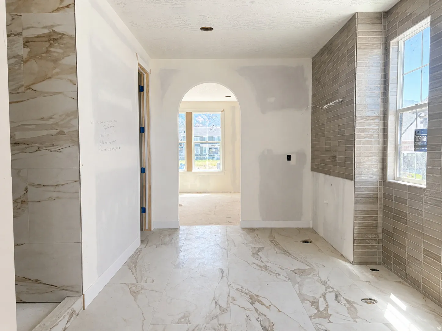 Spacious bath area featuring large format white and brown veined floor tiling, a tiled shower stall with matching veining, and a window with horizontal tile surround