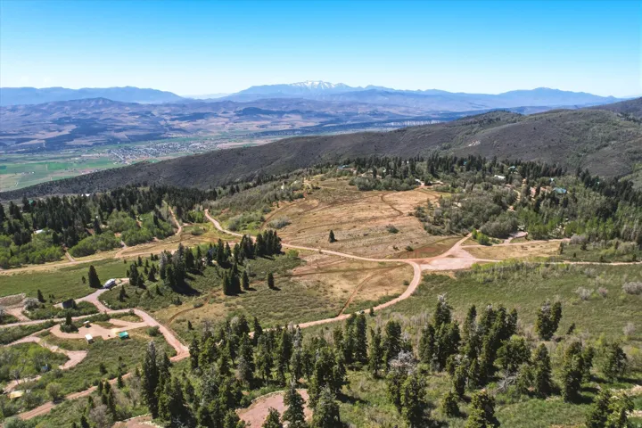 Expansive mountain landscape featuring varied terrain, scattered residential structures, and distant snow-capped peaks