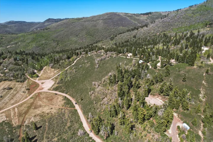 Expansive mountain terrain featuring diverse tree cover, visible dirt roads, and distant structures