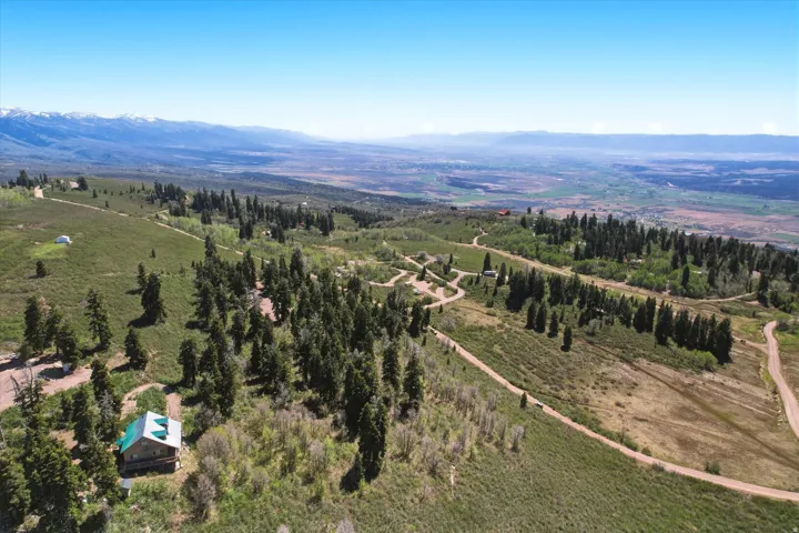 Elevated property featuring a natural landscape with scattered trees, a visible structure with a green roof, and unpaved roads