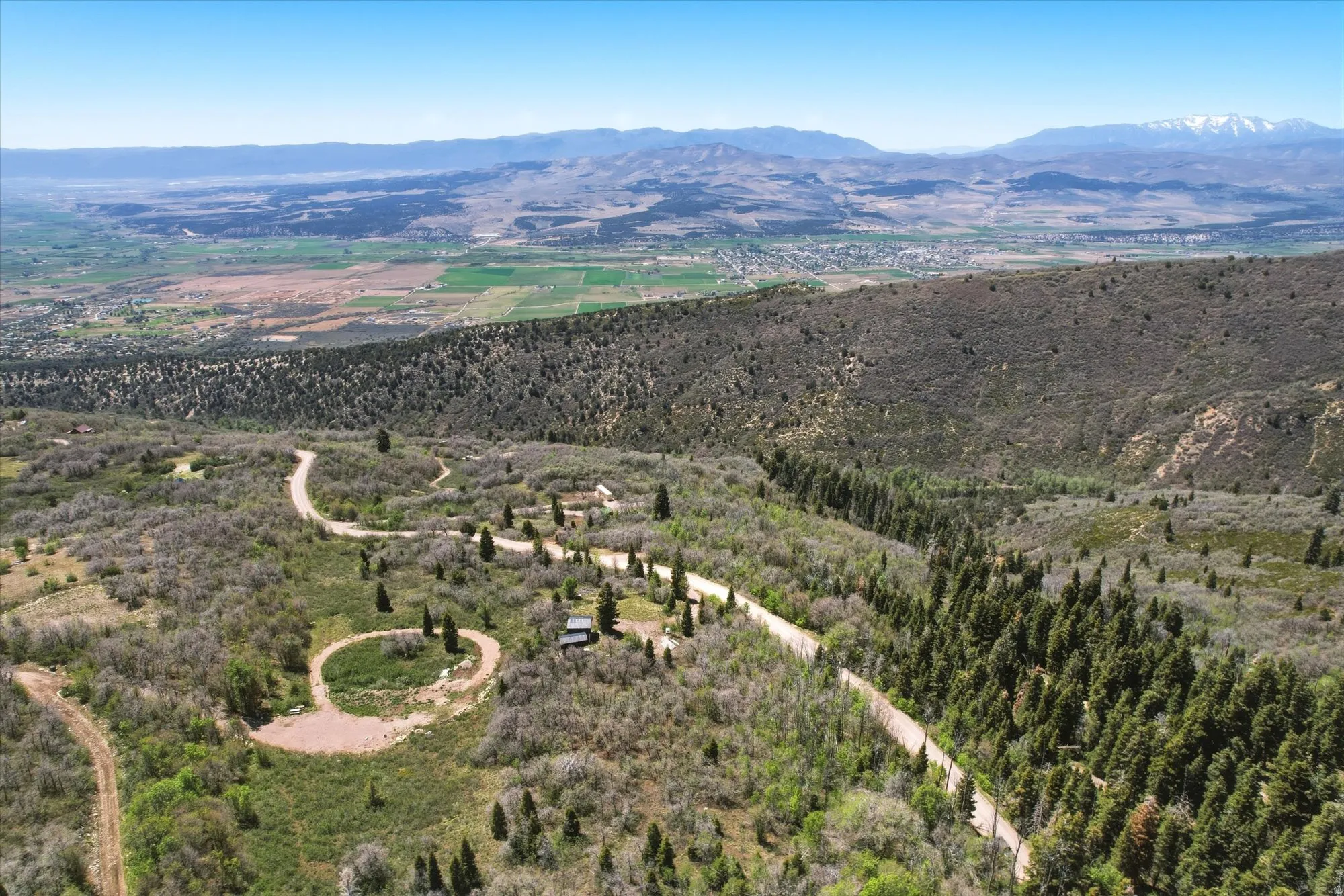 Expansive mountain landscape featuring a winding road, dense evergreen forests, and distant valley views