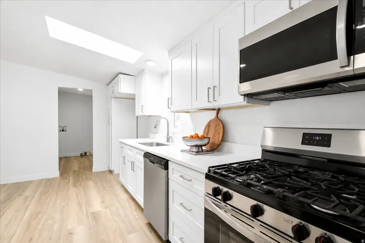 Modern kitchen featuring white cabinetry, light wood-finish flooring, stainless steel appliances, a skylight, and white countertops