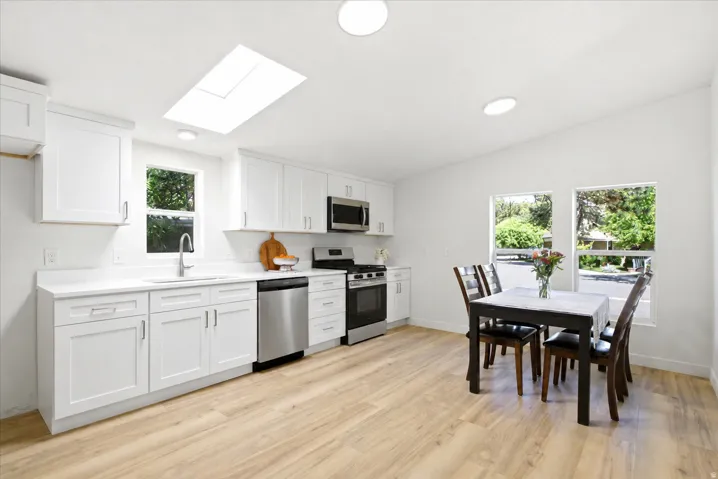 Open-concept kitchen and dining area featuring white cabinetry, stainless steel appliances, wood-finish flooring, a skylight, and recessed lighting