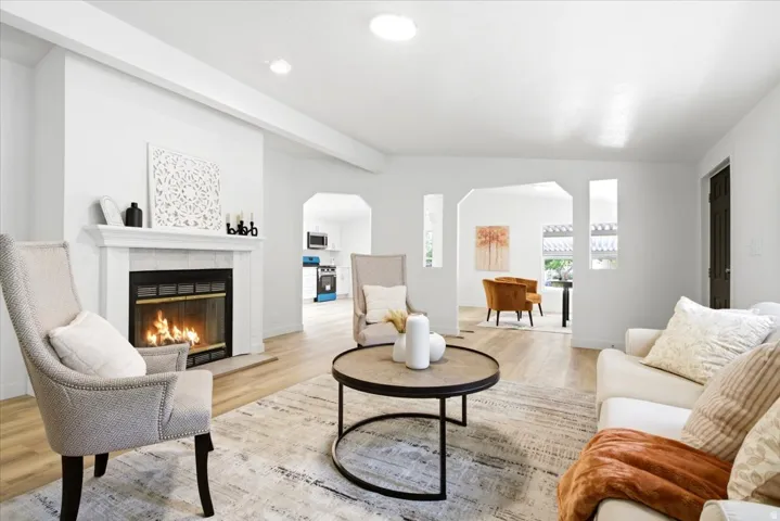 Living room featuring a fireplace with a white mantel, light wood-finish flooring, and arched doorways leading to additional rooms