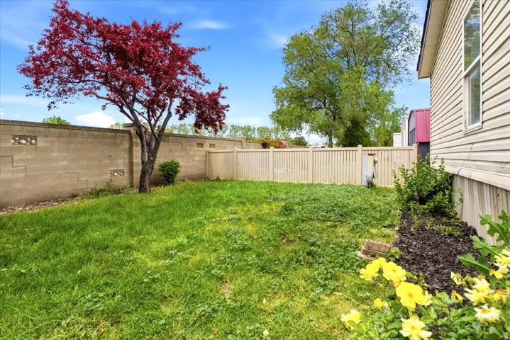 Expansive rear yard featuring green lawn, mature trees, a privacy fence, and a concrete block wall