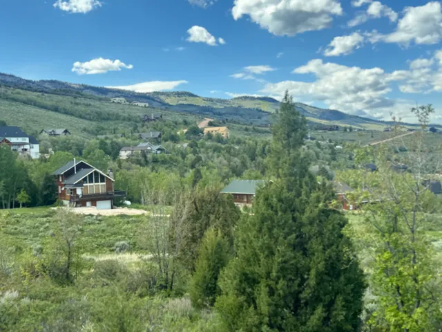 Mountain home featuring a gabled roofline, a second-story balcony, an attached garage, and surrounding natural foliage
