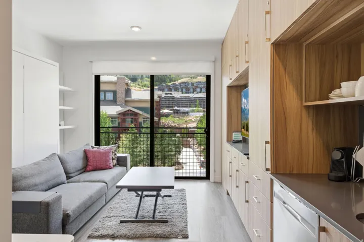 Open-concept living area featuring wood-finish flooring, a full wall of integrated cabinetry with open shelving, and a built-in dishwasher