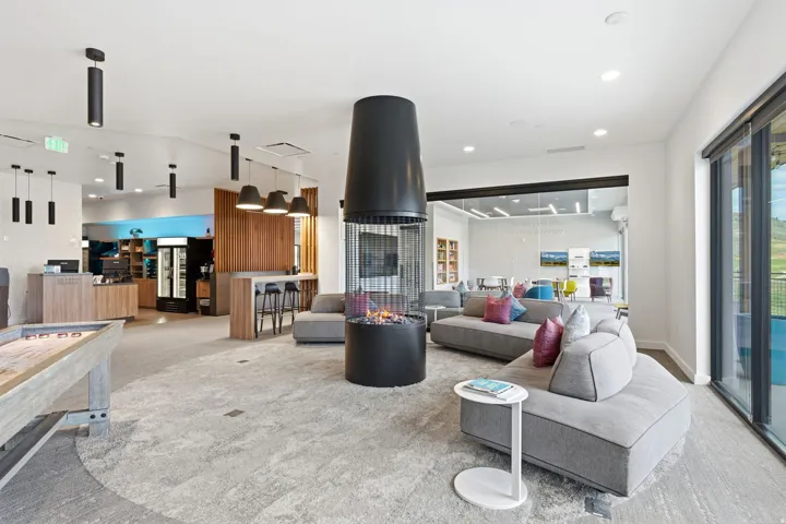 Spacious common area featuring a central cylindrical fireplace, a modern bar area with built-in cabinetry, large format glass doors, and recessed lighting throughout