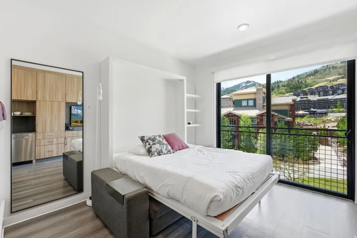 Contemporary studio space featuring a wall-mounted bed, built-in shelving, and wood-finish flooring