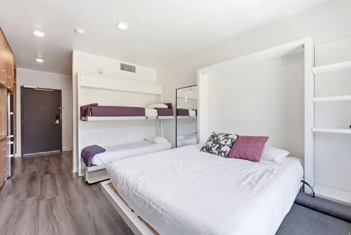 Studio living area featuring a wall-mounted bunk bed system, additional wall-mounted bed, built-in shelving, wood-finish flooring, and recessed lighting
