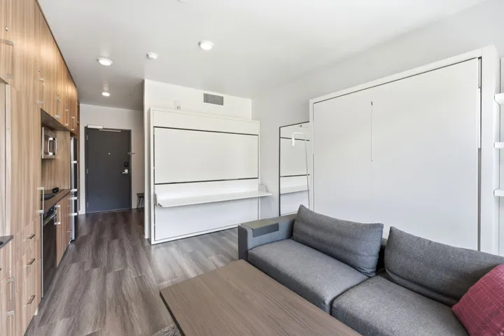 Open-concept living area featuring wood-finish flooring, a built-in wall bed system, a built-in kitchen with wood-finish cabinetry, and recessed ceiling lighting