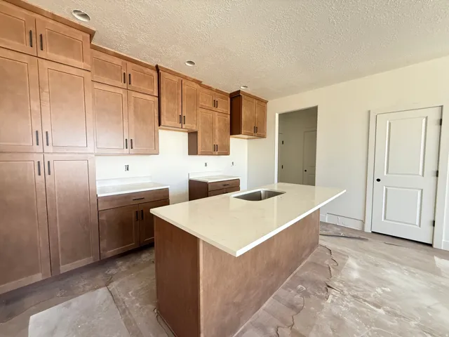 Kitchen featuring extensive wood-finish cabinetry, light-toned countertops, and a central island with an integrated sink