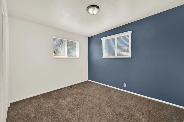 Room featuring two windows with horizontal blinds, a ceiling-mounted light fixture, carpeting, and a contrasting accent wall