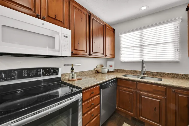 Kitchen featuring wood cabinetry, light-toned countertops, a double basin stainless steel sink, and a window with blinds