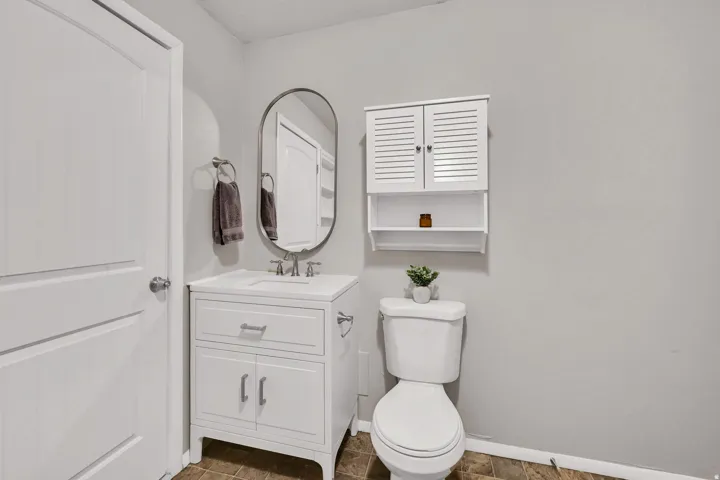 Bathroom featuring a white vanity with integrated sink, oval mirror, wall-mounted storage cabinet, and a white toilet