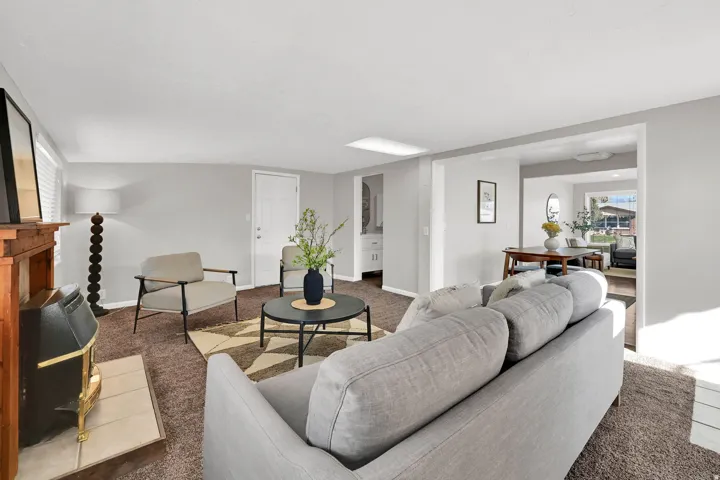 Living room featuring a wood-mantled fireplace, brown carpet, light gray walls, and an entryway door