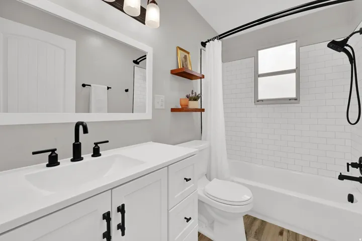 Bathroom featuring a white vanity with integrated sink, black hardware, a large framed mirror, and wood-finish flooring