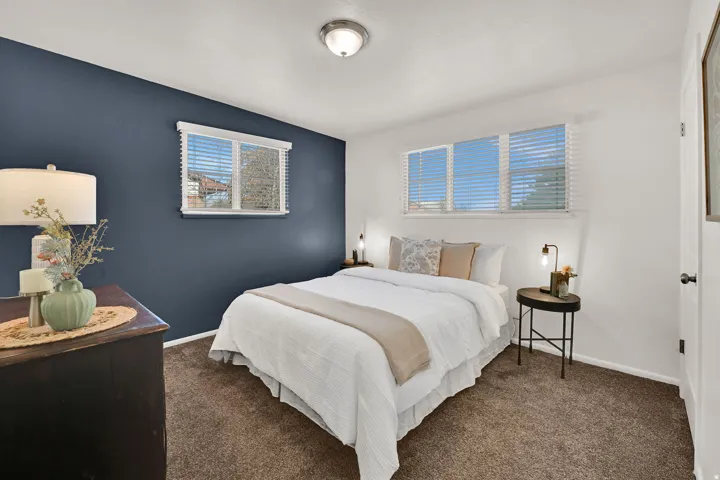 Bedroom featuring dual windows with blinds, a dark accent wall, white walls, and carpeting