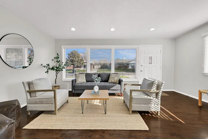 Spacious living area featuring dark wood-finish flooring, a white paneled entry door, recessed ceiling lighting, and multiple large windows with horizontal blinds