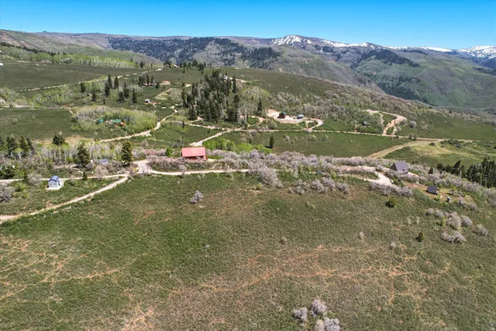 Expansive mountain landscape with multiple dwellings, mature trees, and unpaved roadways