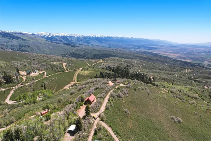 Expansive mountain property with a red-roofed structure, featuring rolling green hills, scattered trees, and distant snow-capped peaks