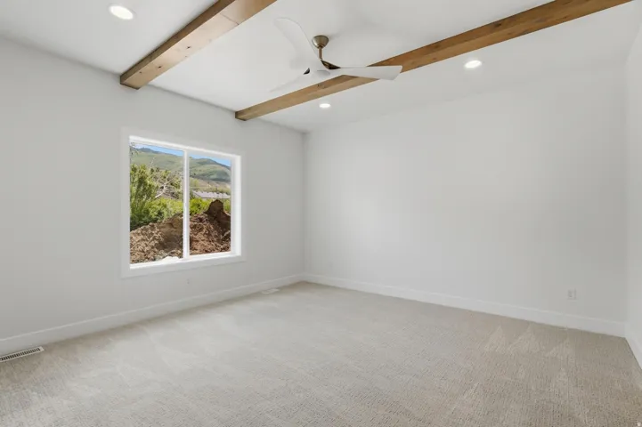 Spacious room featuring exposed wood-finish ceiling beams, recessed lighting, and a modern ceiling fan