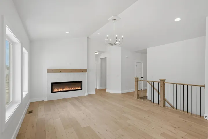 Spacious interior featuring wide plank wood-finish flooring, an electric linear fireplace with tiled surround and wood mantel, recessed lighting, and a modern chandelier