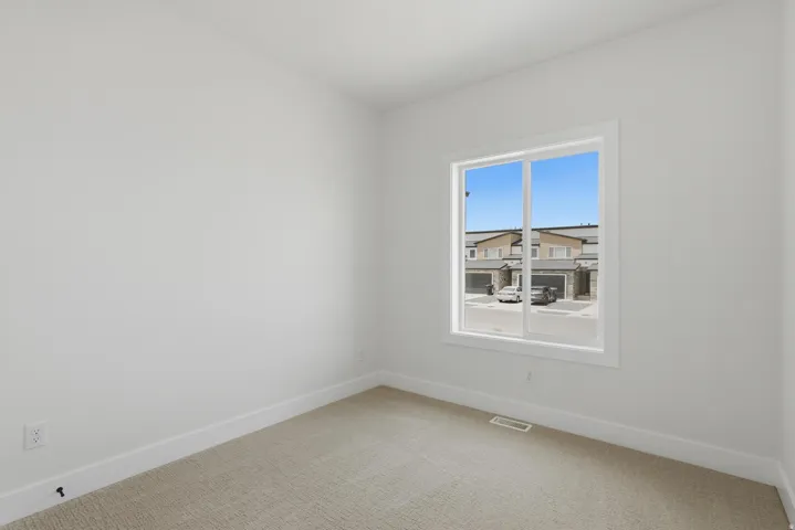 Bright room featuring a large window, neutral carpeting, white baseboards, and a white electrical outlet