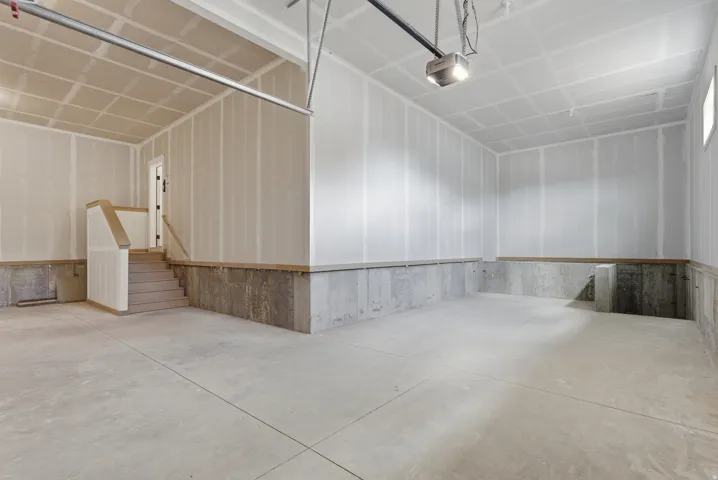 Spacious unfinished garage with concrete flooring, exposed drywall, and a built-in staircase featuring wood-finish handrails and white risers