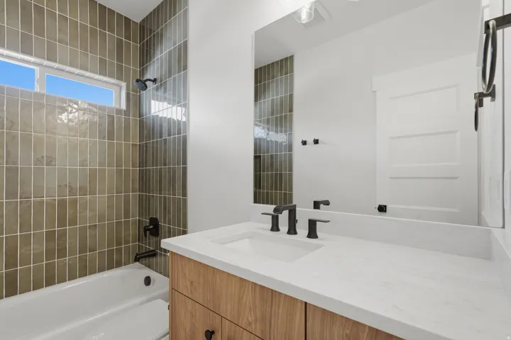 Bathroom vanity featuring a light wood-finish cabinet with black hardware, a white countertop, and an integrated rectangular sink