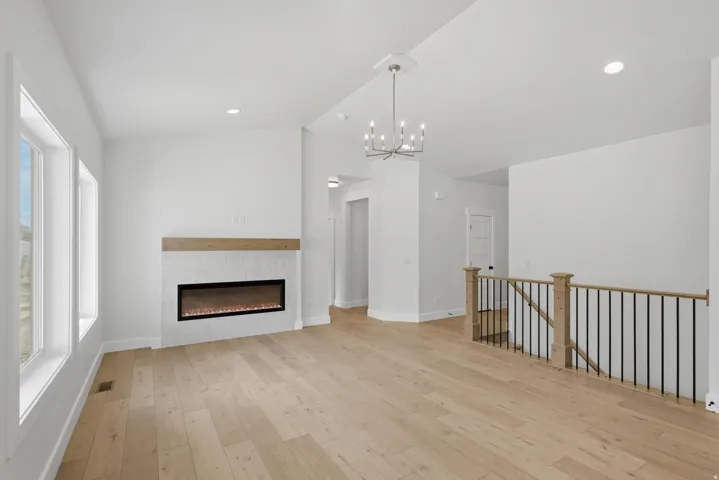 Spacious room featuring light wood-finish flooring, a linear electric fireplace with a wood mantle and tile surround, and multiple windows