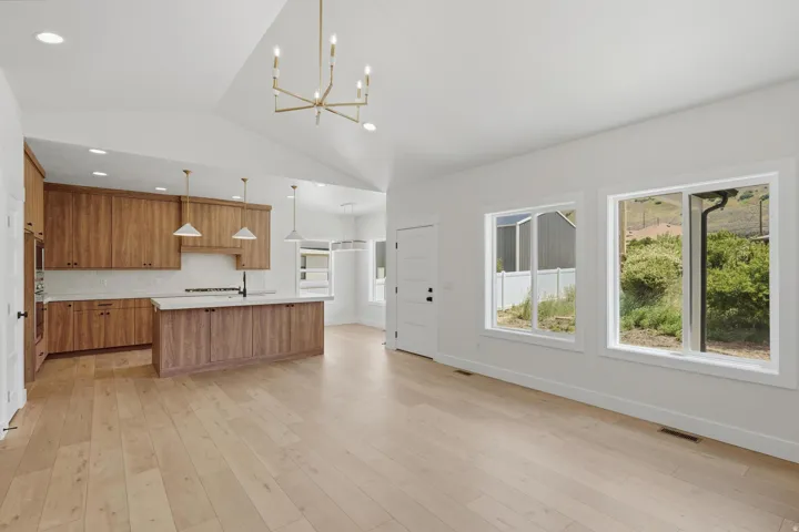Open-concept living area featuring light wood-finish flooring, a vaulted ceiling, and an angular chandelier