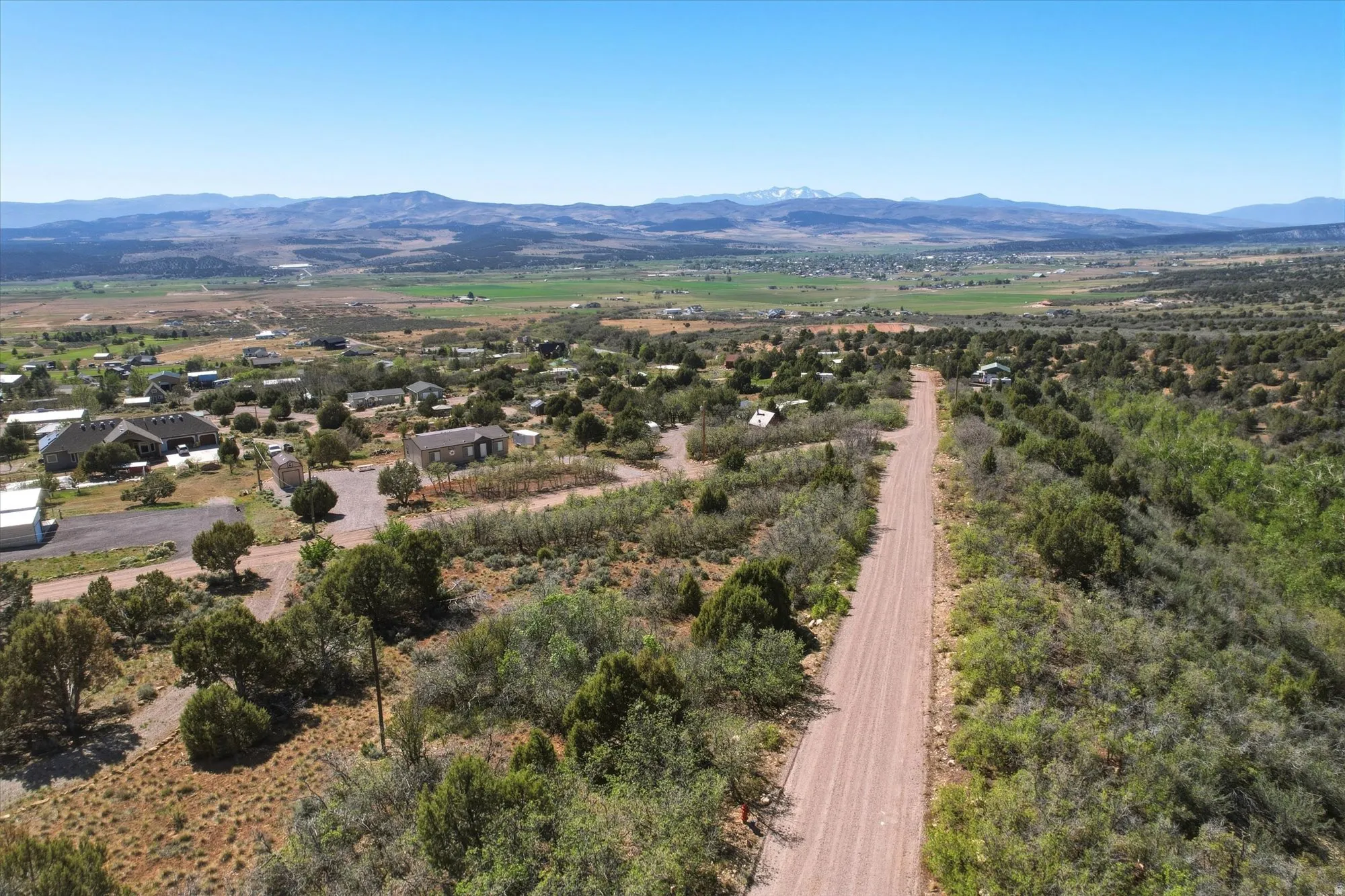 Expansive land parcel featuring a dirt road, varied vegetation including green and arid foliage, and distant mountain ranges under a clear sky