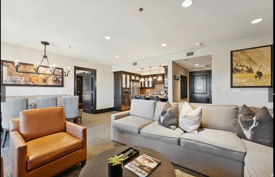 Open-concept living area featuring recessed lighting, a dining area with a linear chandelier, dark-stained trim work, and a kitchen with pendant lighting