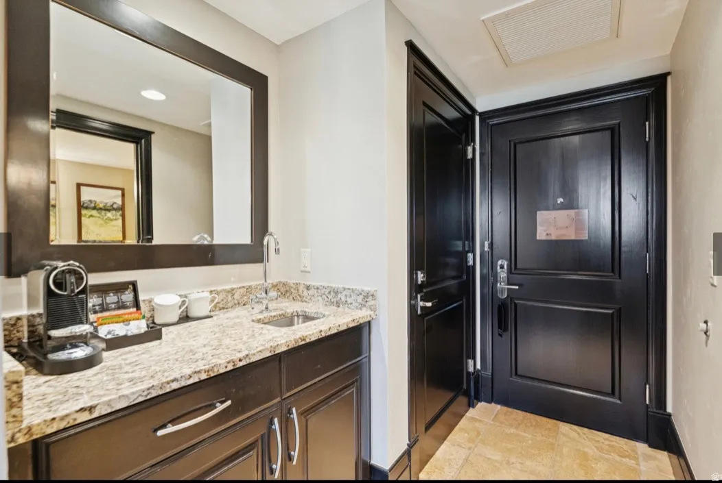 Integrated wet bar with granite countertop, undermount sink, and dark wood-finish cabinetry