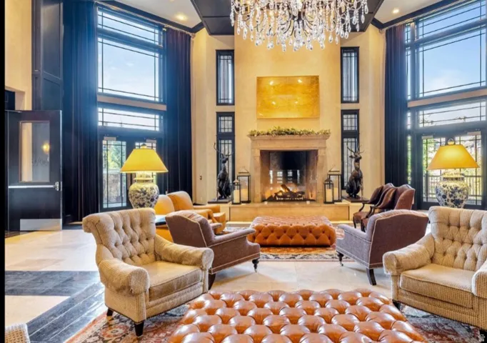 Grand sitting area featuring a prominent fireplace with a stone surround, tall windows with transom detailing, and a multi-tiered crystal chandelier