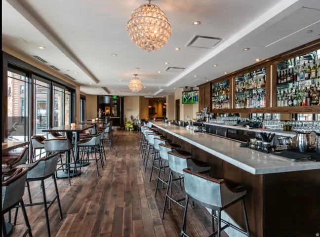 Expansive bar area featuring a long stone-top bar, wood-finish flooring, and multiple crystal chandeliers