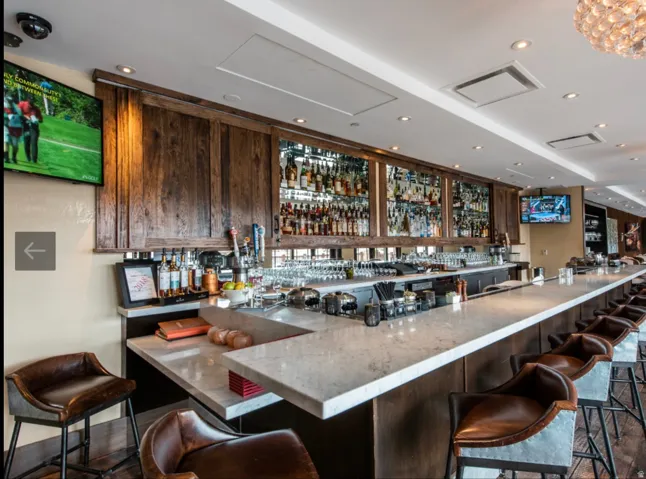 Expansive bar area featuring a light-toned countertop, integrated shelving with mirrored backing, recessed lighting, and wood-finish paneling