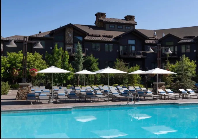 Outdoor swimming pool with lounge chairs and umbrellas, bordered by mature landscaping