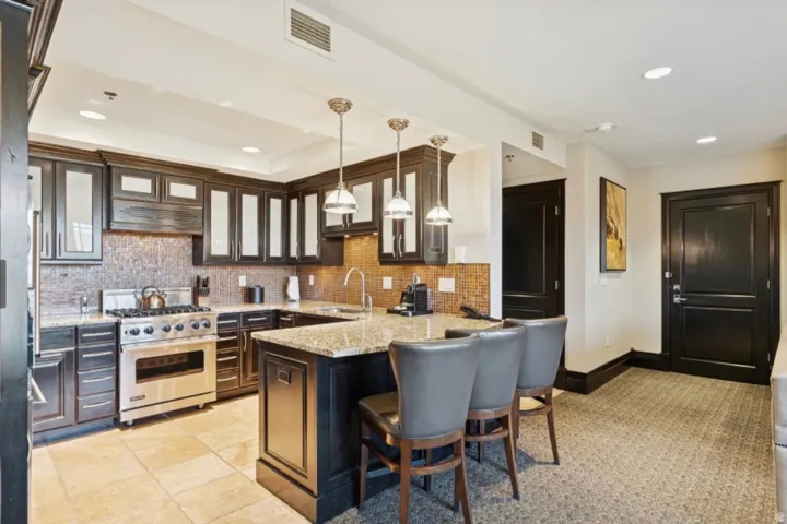 Gourmet kitchen featuring dark wood cabinetry with glass-front uppers, a mosaic tile backsplash, and granite countertops