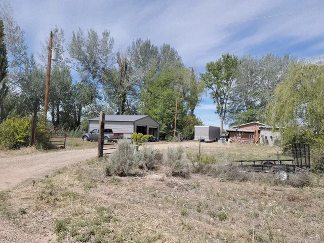 Gated property entrance with a gravel driveway, featuring a two-bay detached garage with a metal roof, and an additional storage structures