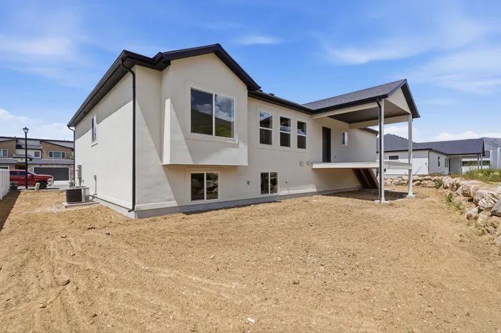 Contemporary rear exterior with a covered upper-level deck, dark shingle roofing, and light-toned stucco siding