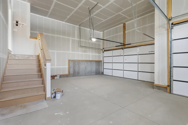 Spacious interior garage featuring a concrete floor, two garage doors, and unfinished drywall