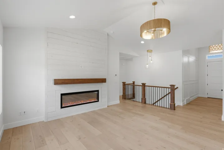 Spacious living area featuring a linear electric fireplace with a wood mantle, shiplap accent wall, and wood-finish flooring