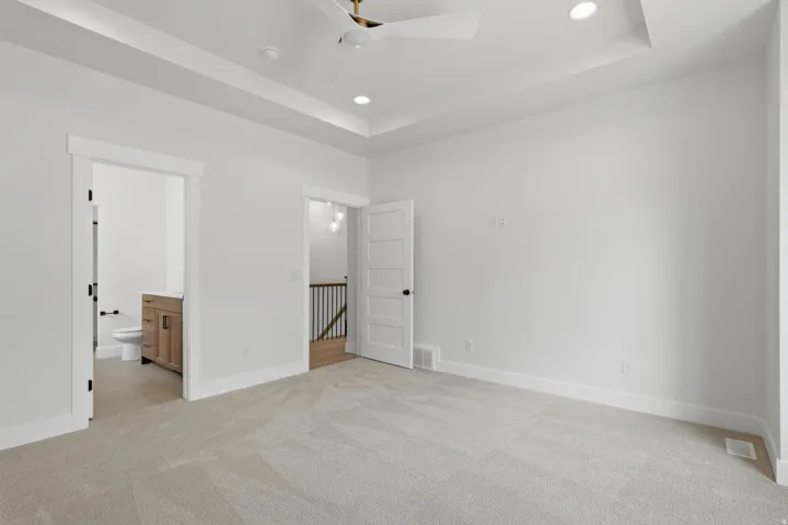Spacious bedroom with light-toned carpeting and a tray ceiling featuring recessed lighting and a ceiling fan