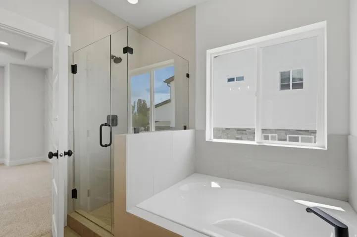 Contemporary bathroom featuring a frameless glass shower enclosure with matte black hardware, a built-in soaking tub, and a large window providing natural light
