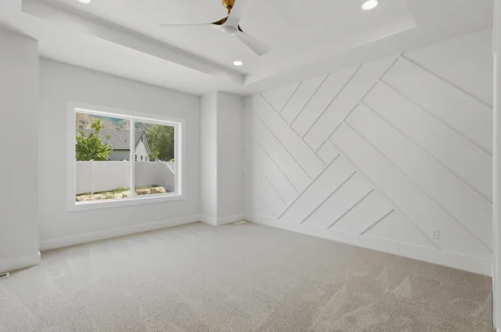 Bedroom featuring a decorative accent wall with geometric paneling, tray ceiling with recessed lighting, and a modern ceiling fan