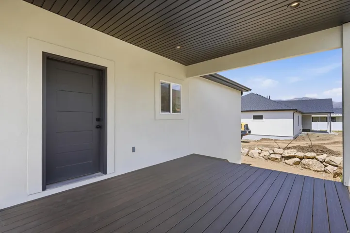 Spacious covered patio featuring durable wood-finish decking, recessed lighting, and a modern paneled door